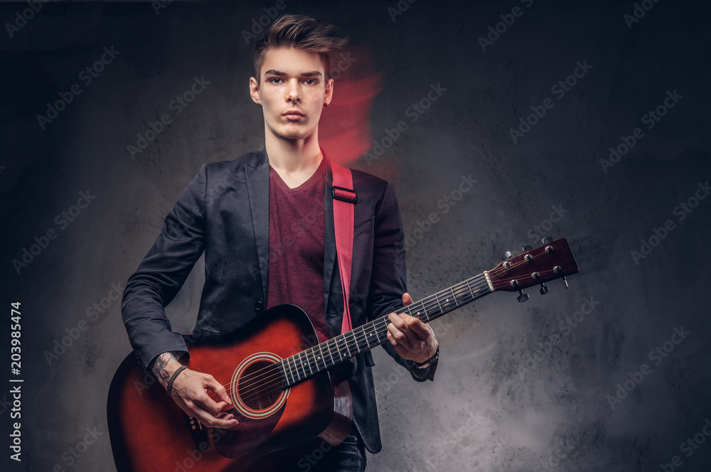 Obraz premium Stylish young musician with stylish hair in elegant clothes, playing on an acoustic guitar.