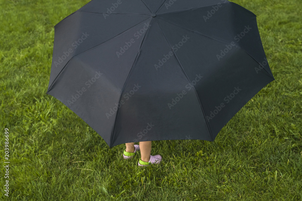 Kid hiding under big umbrella on green grass