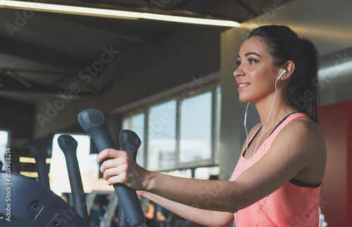 Sporty young woman makes sport exercises on the electrical trainer