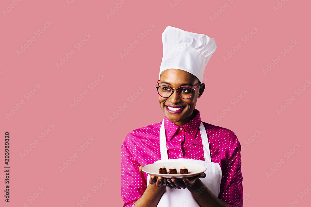 Φωτογραφία Portrait of a smiling young female chef holding a plate with three chocolate pra