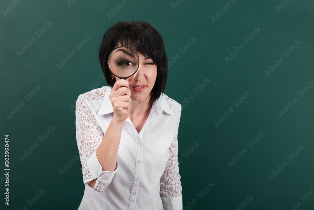 a woman looks forward through a magnifying glass, a blackboard as a background, big eye is visible inside the magnifier, a concept of education and business a woman looks forward through a magnifying glass, a blackboard as a background, big eye is visible inside the magnifier, a concept of education and business