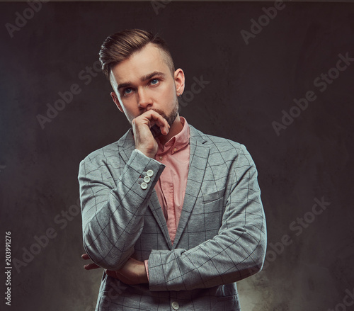 Pensive stylish bearded man with hairstyle and glasses in a gray suit and pink shirt, posing in a studio.