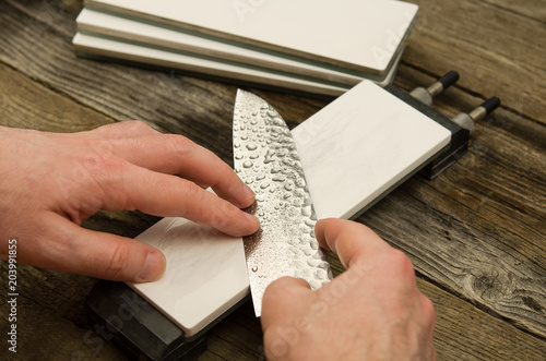Sharpening Japanese knife with glass stone. Santoku knife sharpening. Honing chef knife. Close up of hands sharpening Japanese chef knife. 