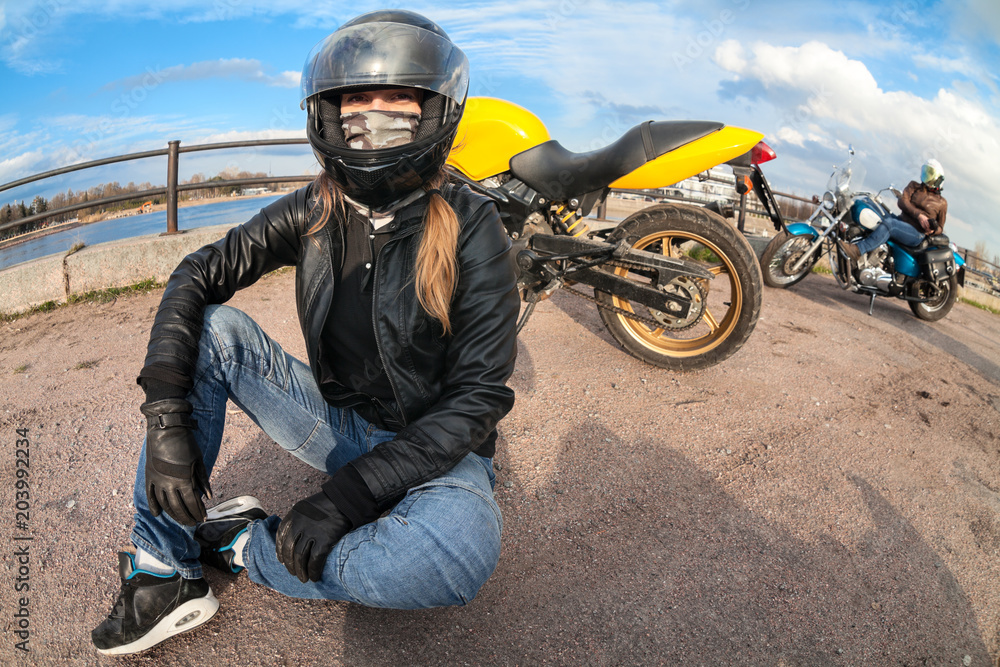Obraz premium Wide angle of girl motorcycle rider sitting on earth next to bike and female biker with chopper on background