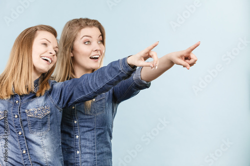 Two happy women friends wearing jeans outfit poitning