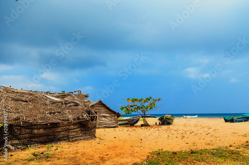Thatched coconut leaf house or fishing hut and boats on tropical beach