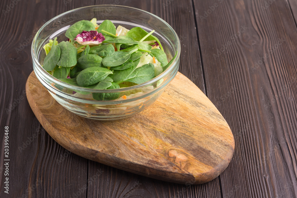 Fresh green salad with spinach, arugula, romaine and lettuce on wooden cutting board. Brown wooden background Fresh green salad with spinach, arugula, romaine and lettuce on wooden cutting board. Brown wooden background
