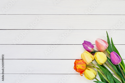 Colorful tulips bouquet on white wooden background. Copy space, top view. Mothers Day, Birthday, Valentines Day concept. Holiday background.