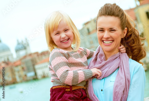 Smiling mother holding happy daughter in Venice on bridge