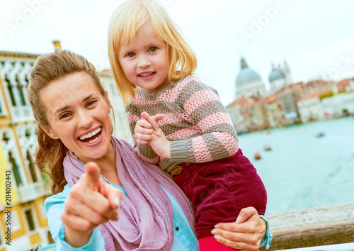 Baby girl and mother poiting in camera while standing on bridge