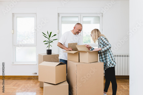 Happy middle aged couple with boxes moving into new home or apartment. Real estate theme.