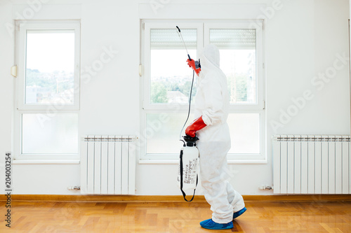 Exterminator in work wear spraying pesticide or insecticide with sprayer.