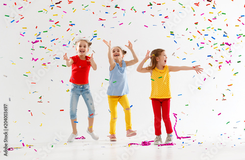 happy children on holidays jumping in multicolored confetti on white