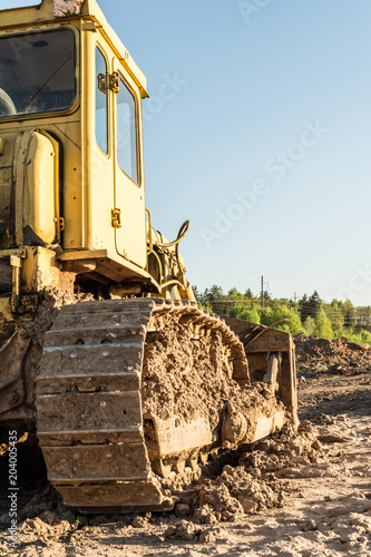 old dirty yellow crawler bulldozer, rear view, the construction machine is lit by the rays of the setting sun