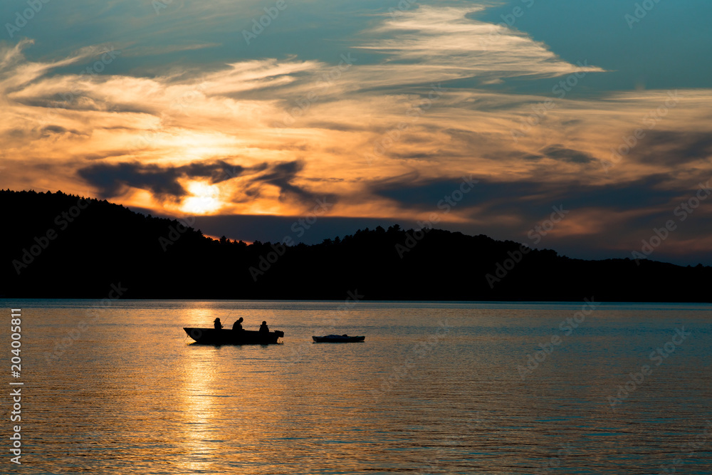 Silhouette of father fishing with children at sunset on a lake