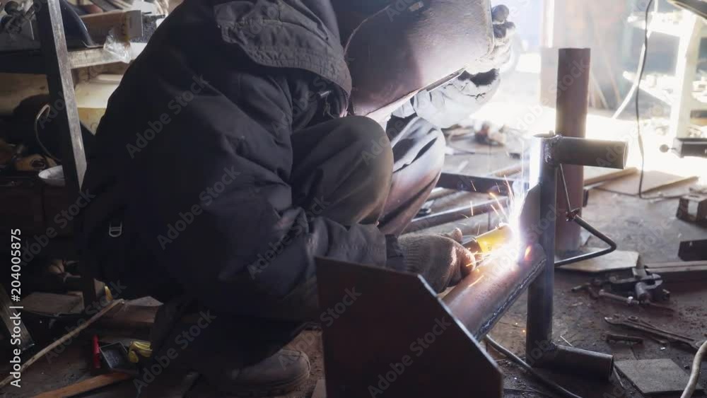 A man welds a metal pipe. Welding of a metal structure in the workshop. A man welds a metal pipe. Welding of a metal structure in the workshop.