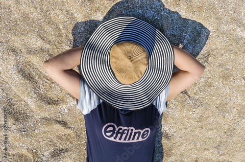 Photography Woman offline and disconnected on the beach sand with hat covering her face