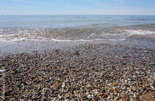 Water washing on shoreline over pebbles on beach on bright sunny day, blue sky in background