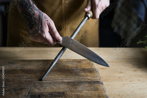 Bilde på lerret Professional chef sharpening knife in the kitchen
