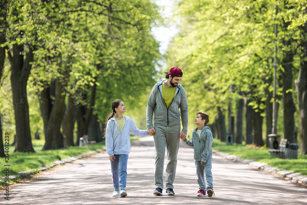 smiling father holding hands of son and daughter and walking in park smiling father holding hands of son and daughter and walking in park