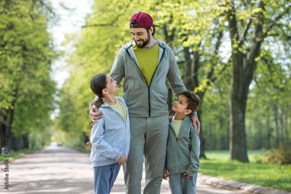 smiling father embracing daughter and son in park smiling father embracing daughter and son in park