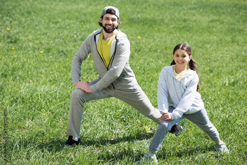 father and daughter doing physical exercise on meadow in park