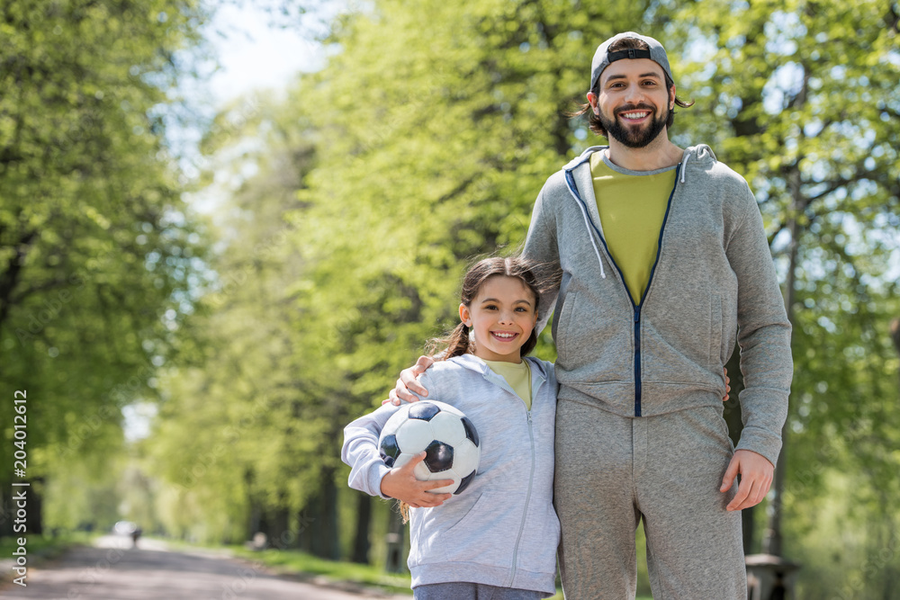 Fototapeta premium smiling father and daughter with ball in park