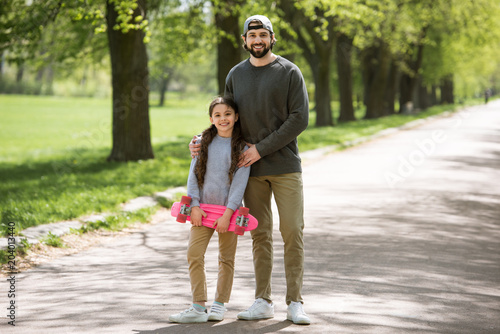 Fototapeta Naklejka Na Ścianę i Meble -  smiling father and daughter holding skateboard in park