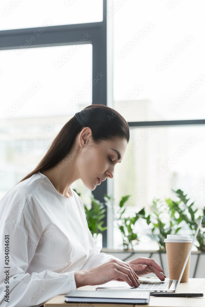 side view of young businesswoman using laptop at workplace side view of young businesswoman using laptop at workplace