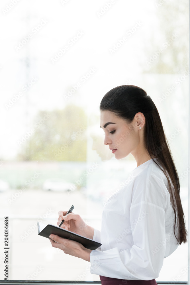 side view of beautiful young businesswoman taking notes in notepad