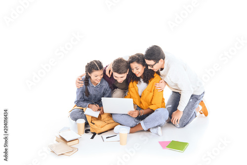 smiling multiethnic students using laptop together isolated on white