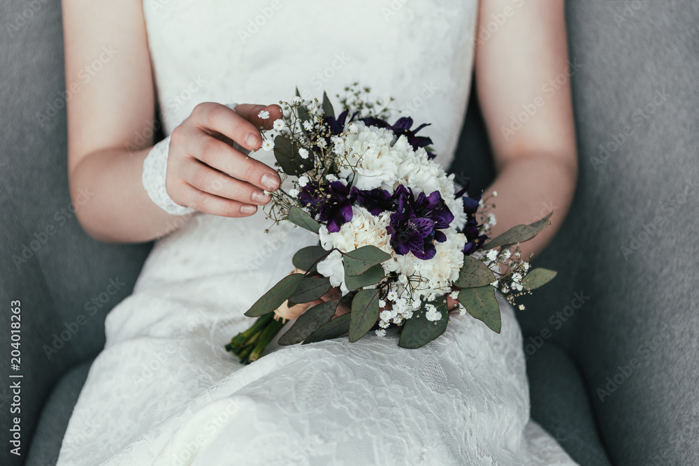 partial view of bride in white dress with beautiful bridal bouquet resting in armchair partial view of bride in white dress with beautiful bridal bouquet resting in armchair