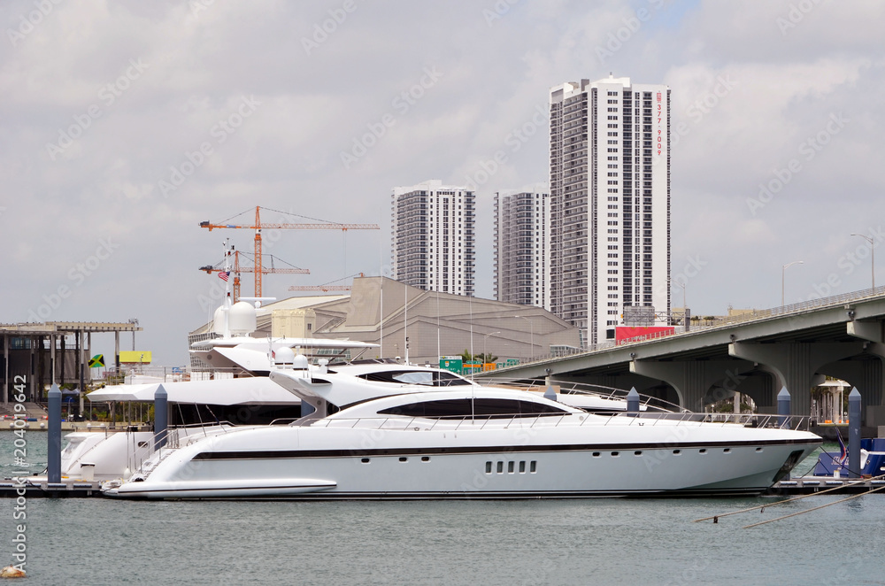 Fototapeta premium Luxury motor yachts moored at a marina near downtown Miami,Florida with tall buildings and tower cranes in the background.