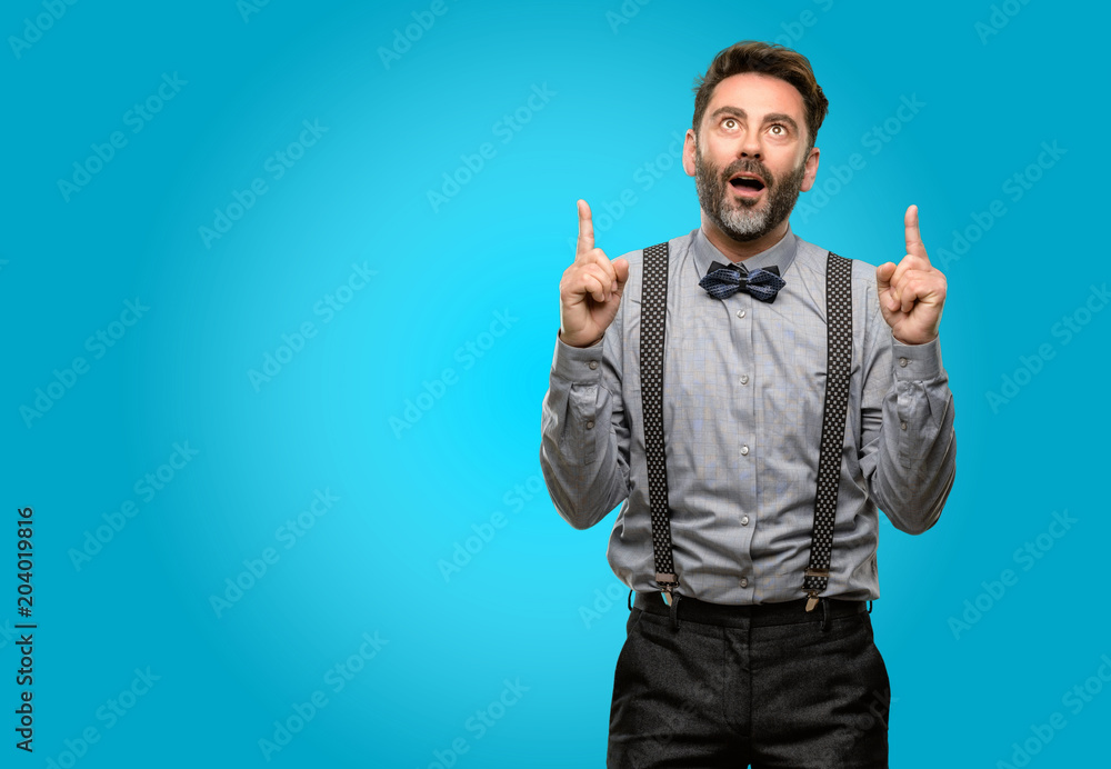 Middle age man, with beard and bow tie happy and surprised cheering expressing wow gesture pointing up Middle age man, with beard and bow tie happy and surprised cheering expressing wow gesture pointing up