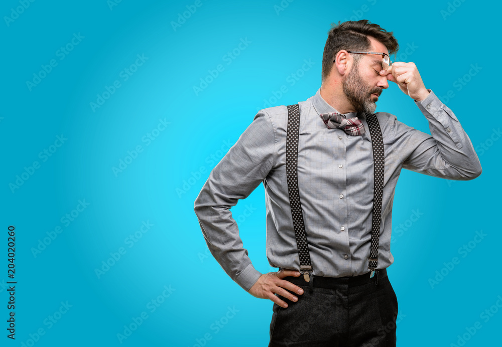 Middle age man, with beard and bow tie with sleepy expression, being overworked and tired, rubbes nose because of weariness Middle age man, with beard and bow tie with sleepy expression, being overworked and tired, rubbes nose because of weariness