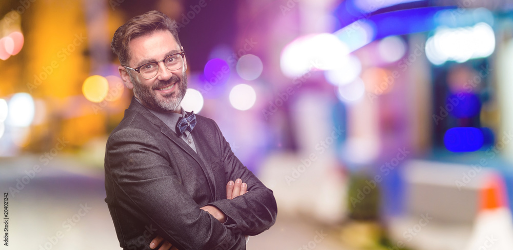 Middle age man, with beard and bow tie with crossed arms confident and happy with a big natural smile laughing at night club Middle age man, with beard and bow tie with crossed arms confident and happy with a big natural smile laughing at night club