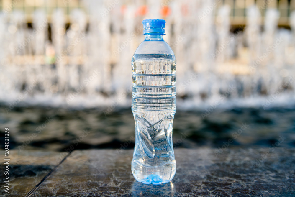 A bottle of drinking water stands on the background of the fountain A bottle of drinking water stands on the background of the fountain