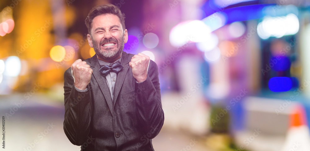 Middle age man, with beard and bow tie happy and surprised cheering expressing wow gesture at night club Middle age man, with beard and bow tie happy and surprised cheering expressing wow gesture at night club