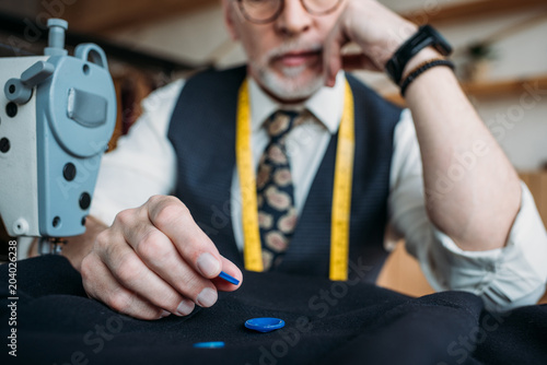 cropped image of senior tailor choosing buttons at sewing workshop