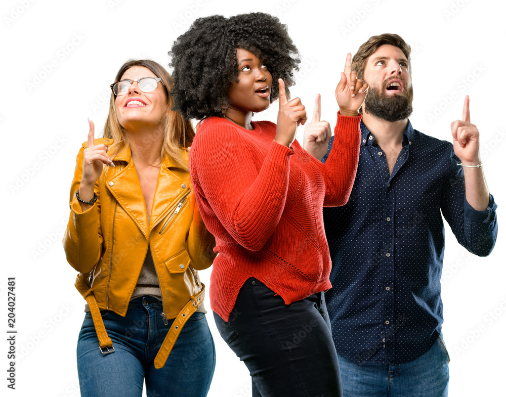 Group of three young men and women happy and surprised cheering expressing wow gesture pointing up Group of three young men and women happy and surprised cheering expressing wow gesture pointing up