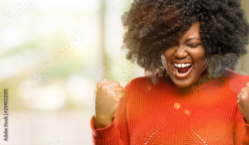 Beautiful african woman happy and excited celebrating victory expressing big success, power, energy and positive emotions. Celebrates new job joyful, outdoor photo