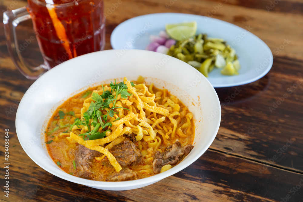Curried noodle soup (Khao soi) with beef and spicy coconut milk on wood table. Thai food cuisine northern style in Chiang Mai. Curried noodle soup (Khao soi) with beef and spicy coconut milk on wood table. Thai food cuisine northern style in Chiang Mai.