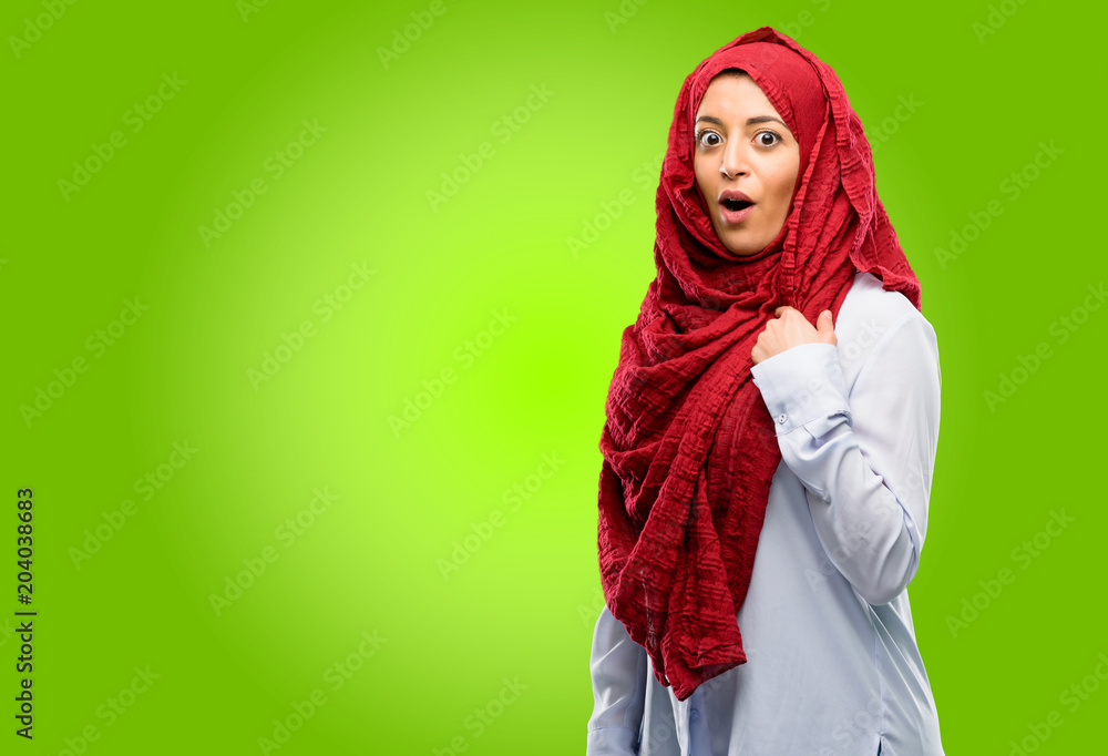 Young arab woman wearing hijab happy and surprised cheering expressing wow gesture, pointing with finger Young arab woman wearing hijab happy and surprised cheering expressing wow gesture, pointing with finger