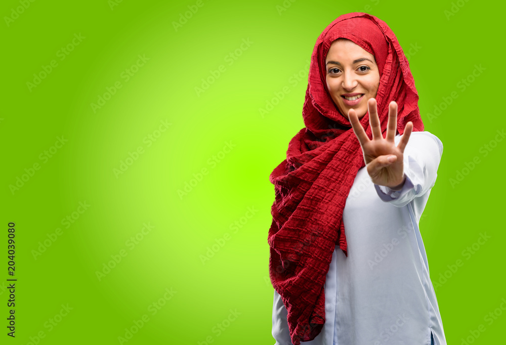 Young arab woman wearing hijab raising his finger, is the number four Young arab woman wearing hijab raising his finger, is the number four