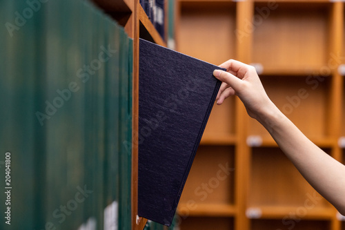 Hand pulling a Thesis book off the shelf in Library. Green colors books.
