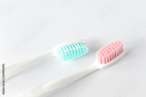 Close up of two plastic white toothbrushes with pink and blue bristle on white background. Free copy space.