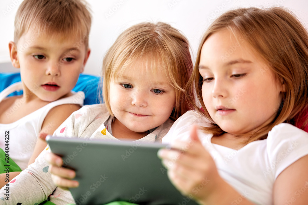 childhood, technology and family concept - little kids with tablet pc computer in bed at home childhood, technology and family concept - little kids with tablet pc computer in bed at home