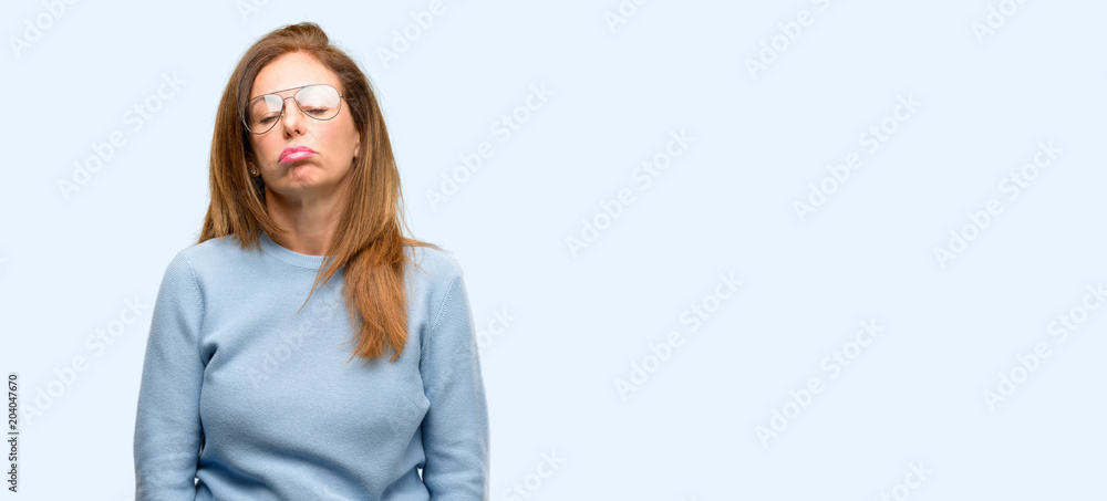 Middle age woman wearing wool sweater and cool glasses with sleepy expression, being overworked and tired isolated blue background Middle age woman wearing wool sweater and cool glasses with sleepy expression, being overworked and tired isolated blue background