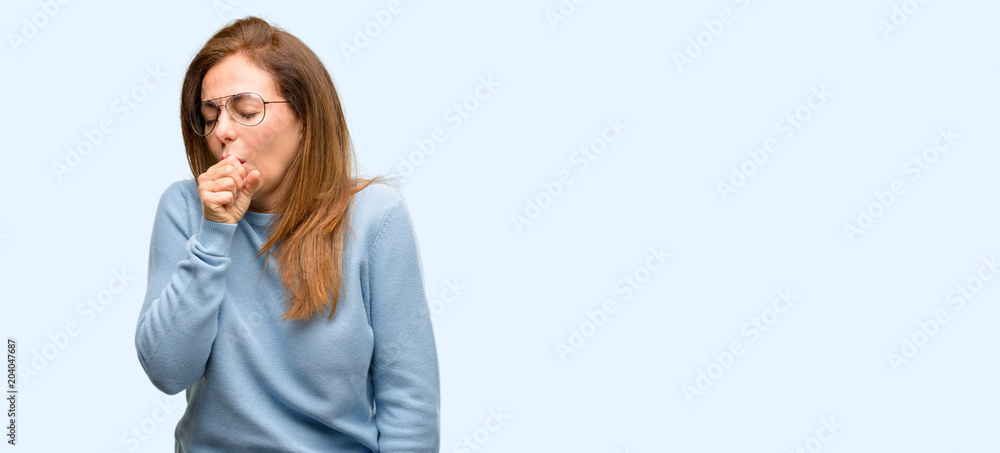 Middle age woman wearing wool sweater and cool glasses sick and coughing, suffering asthma or bronchitis, medicine concept isolated blue background Middle age woman wearing wool sweater and cool glasses sick and coughing, suffering asthma or bronchitis, medicine concept isolated blue background