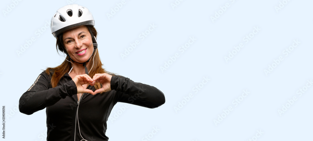 Middle age cyclist woman using earphones happy showing love with hands in heart shape expressing healthy and marriage symbol isolated blue background Middle age cyclist woman using earphones happy showing love with hands in heart shape expressing healthy and marriage symbol isolated blue background